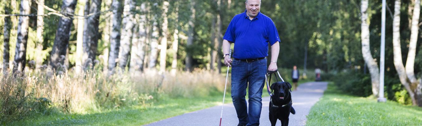 Smiling man with a white cane and a black retriver as a guide dog.
